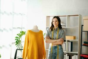 moda progettista donna parlando inteligente Telefono e utilizzando il computer portatile con digitale tavoletta computer nel moderno studio il Abiti sospeso su il cremagliere foto