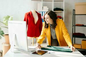 caucasico giovane donna su scrivania nel casa ufficio di moda progettista e detiene tavoletta, il computer portatile e smartphone. foto