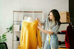 moda progettista donna parlando inteligente Telefono e utilizzando il computer portatile con digitale tavoletta computer nel moderno studio il Abiti sospeso su il cremagliere foto