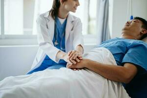 femmina medico Tenere maschio paziente mano su il letto con ricevente soluzione salina soluzione nel ospedale foto
