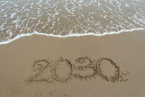 nuovo anno 2030 scritto nel il sabbia su un' spiaggia con mare onda sfondo. foto