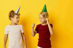 piccolo bambini vacanza divertimento con caps su il tuo testa giallo sfondo foto