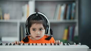 asiatico carino ragazza indossare cuffie apprendimento in linea pianoforte musica con insegnante di mobile Telefono o tavoletta. il idea di attività per il bambino a casa durante quarantena. musica apprendimento studia concetto. foto