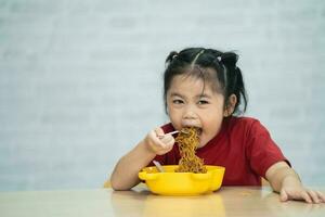 asiatico bambino ragazza godere contento utilizzando posate cucchiaio e forchetta mangiare delizioso spaghetto nel cucina su cenare tavolo. contento asiatico bambino ragazza pratica mangiare di sua se stesso su cenare tavolo. bambino cibo concetto foto