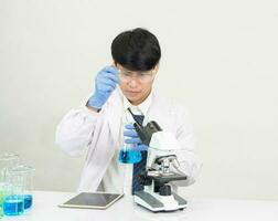 asiatico maschio alunno scienziato indossare un' medico toga nel il laboratorio guardare a il chimico. causato di miscelazione reagenti nel scientifico ricerca laboratori con test tubi e microscopio su il tavolo foto