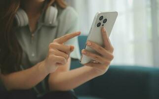 contento asiatico adolescente ragazza Tenere tampone computer aggeggio utilizzando digitale tavoletta tecnologia seduta su il divano a casa. sorridente giovane donna utilizzando app, shopping in linea, lettura notizia, navigazione Internet su divano foto