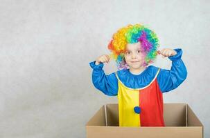 ragazzo di cinque anni vestito nel il costume di un' clown soggiorni nel un' scatola di cartone carta scatola. foto