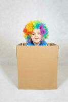 ragazzo di cinque anni vestito nel il costume di un' clown soggiorni nel un' scatola di cartone carta scatola. foto