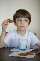 ragazzo di sei anni è assunzione un' bicchiere di caldo latte con avena biscotti. foto