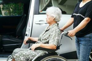 il caregiver aiuta il paziente con disabilità della donna anziana asiatica a salire nella sua macchina, concetto medico. foto