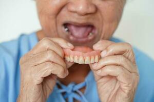 asiatico anziano donna paziente indossare denti dentiera in sua bocca per masticare cibo. foto