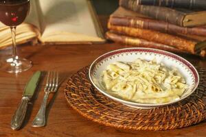 bellissima piatto di penne con bianca formaggio salsa. nel il sfondo vecchio libri foto