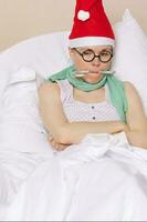 malato giovane signora nel un' Babbo Natale cappello e caramella soggiorni nel sua letto foto