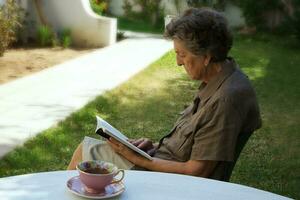 un vecchio donna è lettura un' libro nel il giardino foto