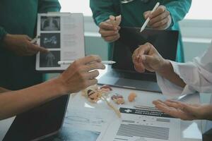 multirazziale squadra di medici discutere un' paziente in piedi raggruppati nel il foyer guardare a un' tavoletta computer, vicino su Visualizza foto