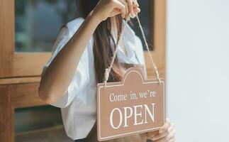 benvenuto. aprire. barista, cameriera donna svolta Aperto cartello tavola su bicchiere porta nel moderno bar caffè negozio pronto per servizio, bar ristorante, Al dettaglio negozio, piccolo attività commerciale proprietario, cibo e bevanda concetto foto