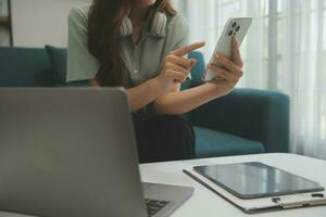 contento asiatico adolescente ragazza Tenere tampone computer aggeggio utilizzando digitale tavoletta tecnologia seduta su il divano a casa. sorridente giovane donna utilizzando app, shopping in linea, lettura notizia, navigazione Internet su divano foto