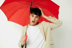 ritratto di un' giovane uomo Tenere un ombrello nel il mani di in posa moda leggero sfondo inalterato foto