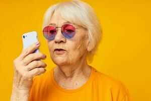 ritratto di un vecchio amichevole donna nel alla moda bicchieri con un' smartphone isolato sfondo foto