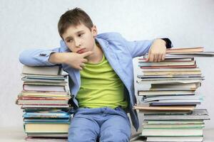 triste pensieroso ragazzo alunno si siede fra pile di libri. acquisire conoscenza. stanco alunno. foto