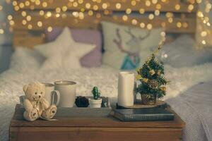 Natale accogliente interno sfondo. un' letto, un' tavolo con un' tazza e un' giocattolo, un' poco a spina di pesce e bokeh luci. foto