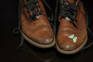 un' paio di Marrone Vintage ▾ pelle scarpe con un' farfalla spilla su un' buio sfondo. bellissimo pelle scarpe. retrò scarpe. foto