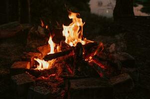 un' falò nel avvicinamento, fiamme, carbonizzato pezzi di logs e cenere nel il Aperto aria contro il paesaggio. campeggio. foto