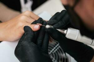 un' avvicinamento di un' manicure maestro in lavorazione il chiodo superficie con un' fresa su un elettrico macchina, rimozione sbavature. il concetto di un' professionale manicure salone foto