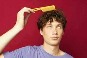 ritratto di un' giovane Riccio uomo in posa spazzola per capelli personale cura rosso sfondo foto