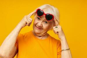 sorridente anziano donna nel casuale maglietta occhiali da sole giallo sfondo foto
