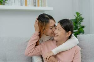 madre giorno, carino asiatico adolescente ragazza abbracciare e baci su il guancia, maturo mezzo età mamma. amore, bacio, cura, contento Sorridi godere famiglia volta. celebrare speciale occasione, contento compleanno, allegro Natale. foto