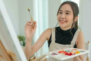 bellissimo femmina Hobby di artista e uso pennello nel astratto arte per creare capolavoro. pittore dipingere con acquerelli o olio nel studio Casa. godere pittura come passatempo, ricreazione, ispirazione foto