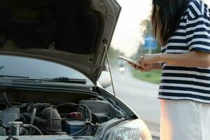 guasto, rotto macchina, riparazione. donna usi mobile Telefono dai un'occhiata assicurazione premi attraverso applicazione dovuto per auto incidente . trova box auto per ottenere auto fisso durante nazione tour, in attesa per aiuto, emergenza. foto