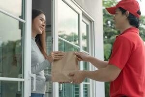 contento sorridente asiatico donna riceve carta Borsa pacco di cibo a partire dal Corriere davanti Casa. consegna uomo Spedire consegnare esprimere. in linea acquisti, carta contenitore, porta via, postino, consegna servizio, pacchi foto