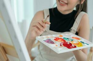 professionale femmina artista ragazza uso pennello nel astratto arte per creare capolavoro. pittore dipingere con acquerelli o olio nel studio Casa. bellissimo donna godere pittura come passatempo. opera ricreazione foto