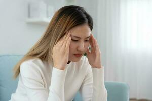 male alla testa, femmina avendo emicrania dolore, cattivo Salute, asiatico donna sensazione fatica e male alla testa, ufficio sindrome, triste stanco toccante fronte avendo emicrania o depressione, irritata ragazza, tristezza dolore foto