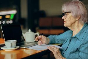 anziano donna seduta nel un' bar con un' tazza di caffè e un' il computer portatile pensionato donna chat inalterato foto