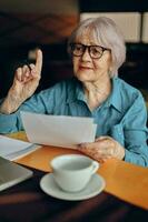 contento anziano donna seduta nel un' bar con un' tazza di caffè e un' il computer portatile stile di vita inalterato foto