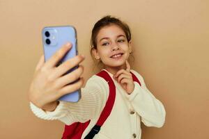 ritratto di contento sorridente bambino ragazza con Telefono in posa rosso zaino isolato sfondo foto