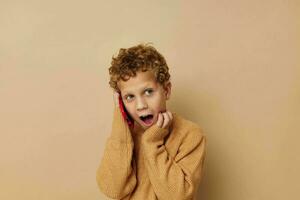 Riccio ragazzo parlando su il Telefono in posa beige sfondo foto