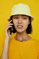 giovane donna nel un' giallo cappello gioventù stile casuale parlando su il Telefono isolato sfondo foto