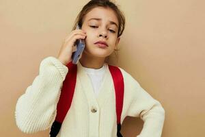 carino ragazza parlando su il Telefono con un' zaino infanzia inalterato foto