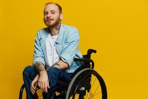 un' uomo nel un' sedia a rotelle Sorridi e felicità, pollice su, con tatuaggi su il suo mani si siede su un' giallo studio sfondo, il concetto di Salute un' persona con disabilità foto