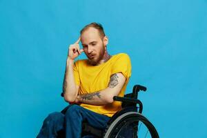 un' uomo si siede nel un' sedia a rotelle premura nel un' maglietta su un' blu sfondo nel il studio, il concetto di un' gratuito senza barriere ambiente per persone con disabilità foto