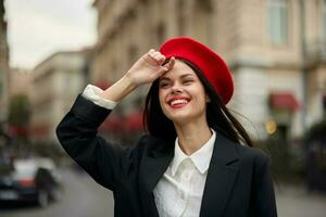 moda donna ritratto Sorridi con denti in piedi su il strada nel davanti di il città turista nel elegante Abiti con rosso labbra e rosso berretto, viaggiare, cinematico colore, retrò Vintage ▾ stile, urbano moda. foto