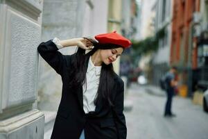 donna in piedi vicino un' parete nel il città indossare un' elegante giacca e rosso berretto con rosso labbra, viaggio e tempo libero, francese stile di vestire. foto