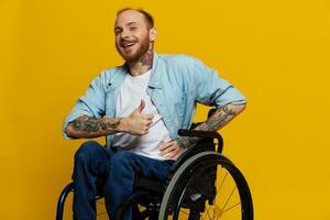 un' uomo nel un' sedia a rotelle Sorridi e felicità, pollice su, con tatuaggi su il suo mani si siede su un' giallo studio sfondo, il concetto di Salute un' persona con disabilità foto