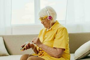 contento anziano donna guardare in sua Telefono video chiamata con cuffie Sorridi, tecnologia per comunicazione, luminosa moderno interno, stile di vita in linea comunicazione foto