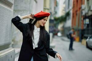 donna in piedi vicino un' parete nel il città indossare un' elegante giacca e rosso berretto con rosso labbra, viaggio e tempo libero, francese stile di vestire. foto