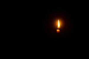 un' singolo ardente candela fiamma o leggero raggiante su un arancia candela su nero o buio sfondo su tavolo nel Chiesa per Natale, funerale o memoriale servizio con copia spazio. foto